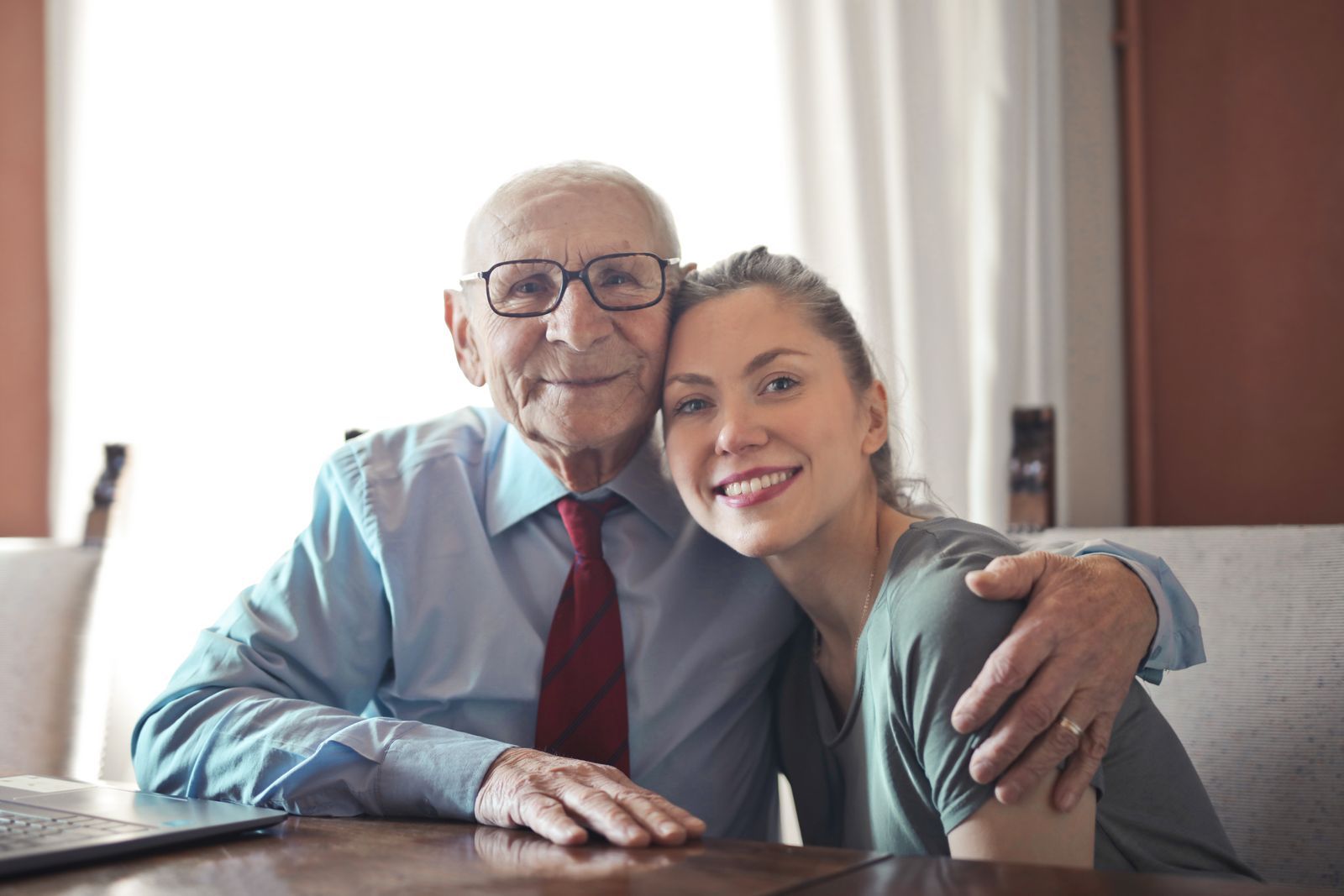 An older man and a younger woman smiling together at a table at home