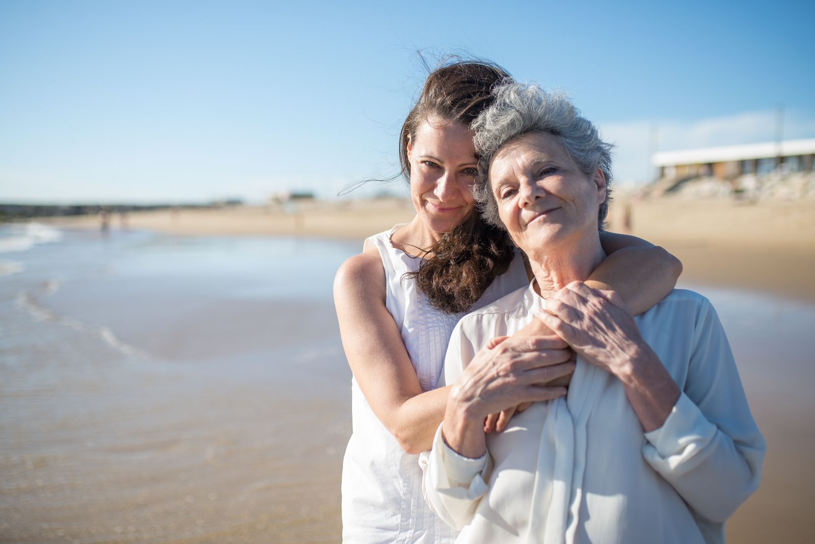 A younger woman hugging an older woman on a sunny beach